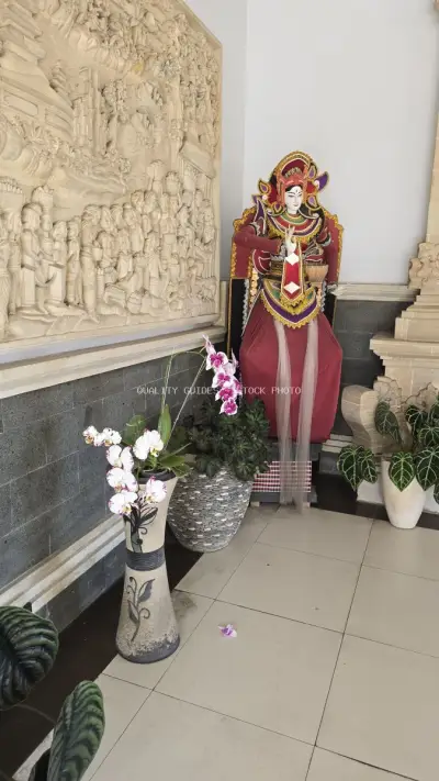 Balinese Temple Statue with Orchid Flowers and Stone Carvings - stock photo
