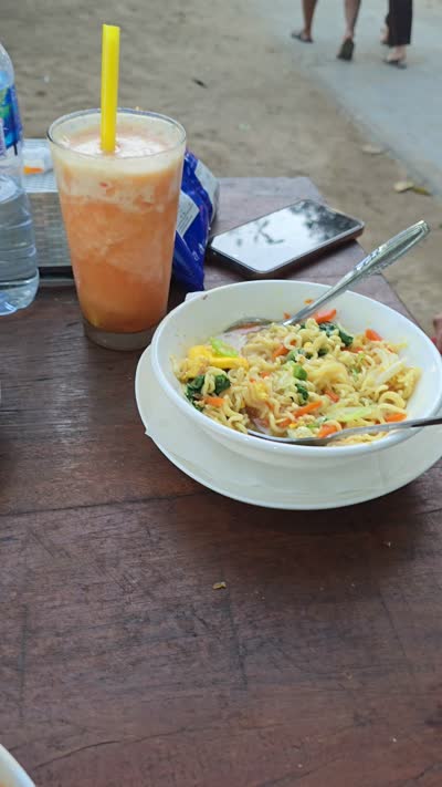 Vertical footage of local food and drinks on a wooden table at a Bali beach bar, panning to show the sandy outdoor dining area and colorful bar stall. - stock photo