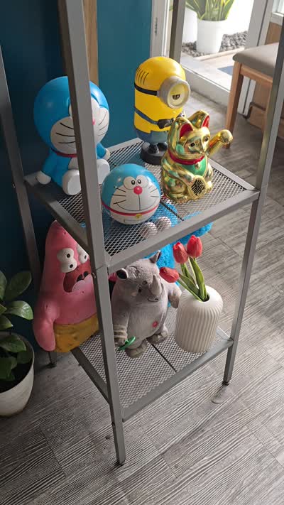Upward pan of quirky cartoon character figurines and cafe decor on a metal shelf, revealing a bright street view outside a window. - stock photo