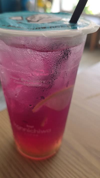 Pink iced drink with condensation and black straw on a wooden table in a cafe, Bali. - stock photo