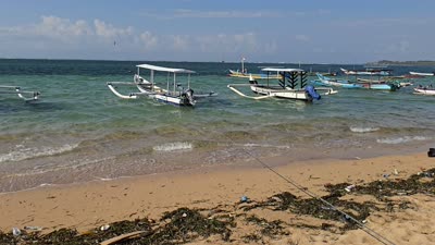 Traditional Balinese jukung boats anchored in turquoise water at Pantai Bopel beach, Bali, with sand and debris in the foreground. - stock photo