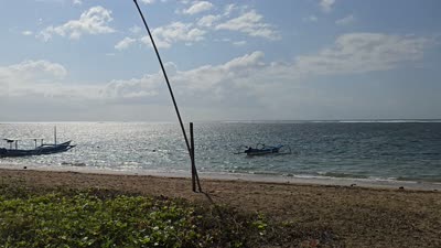 Coastal path with people, traditional boats on Karang Beach, Bali, and a tropical garden with a villa. - stock photo