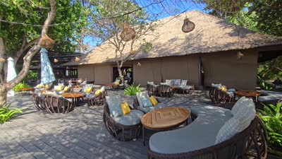 Beachfront restaurant and traditional boats on a sunny Bali beach with people walking. - stock photo
