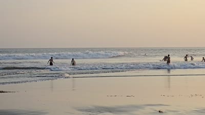 Sunset beach footage in Bali with silhouetted people, surfers, and golden reflections on wet sand. - stock photo