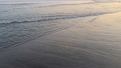 Golden hour sunset over Echo Beach in Canggu, Bali, with gentle ocean waves on dark sand and distant beachgoers. - stock photo