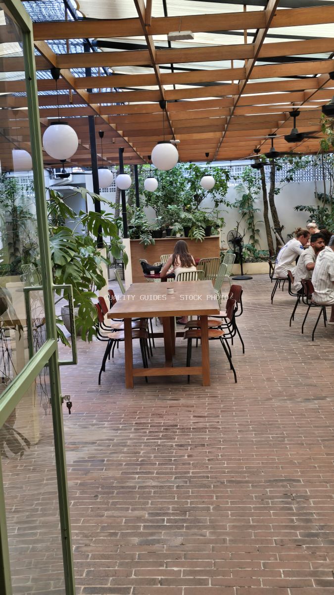 Outdoor cafe in Bali with wooden pergola, plants, brick floor, and people dining. - stock photo