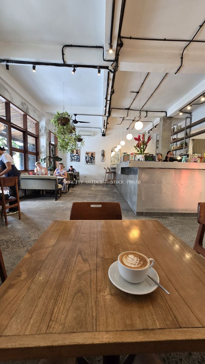 Latte on a wooden table in a modern industrial cafe with people in the background. - stock photo
