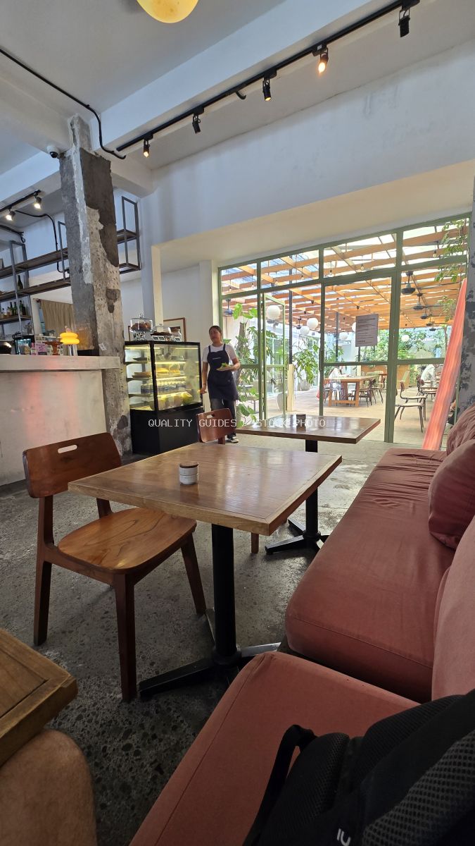 Interior of a modern cafe in Bali with wooden tables, pink sofa, and staff member. - stock photo