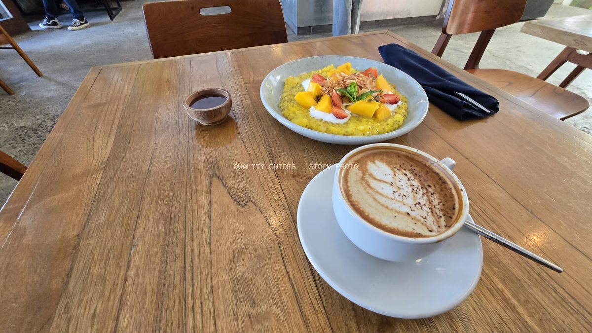 Healthy breakfast bowl with mango and strawberries, latte, and syrup on a wooden table in a cafe. - stock photo