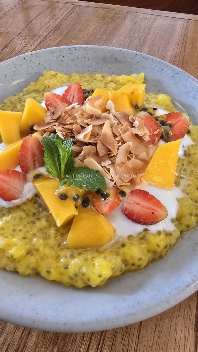 Close-up of a colorful tropical chia pudding with mango, strawberries, coconut, and mint on a wooden table. - stock photo