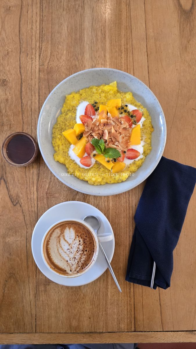 Overhead view of a tropical fruit breakfast bowl, latte, and coffee on a wooden table. - stock photo