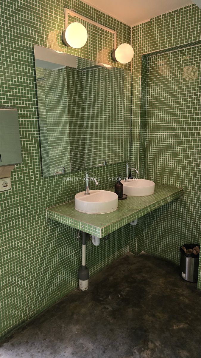 Modern public restroom with green mosaic tiles, double sinks, mirror, and round lights. - stock photo
