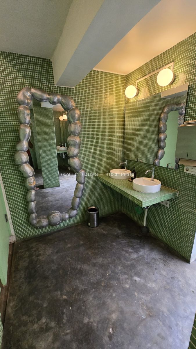 Modern bathroom with vibrant green mosaic tiles, two white sinks, and a large, irregularly shaped mirror. - stock photo