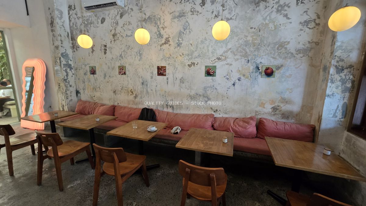 Interior of a modern rustic cafe with pink bench seating, wooden tables, and warm globe lights on a textured wall. - stock photo