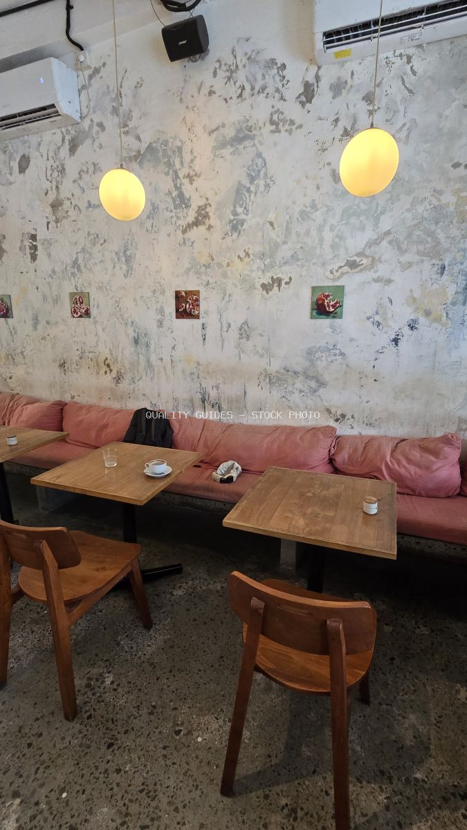 Interior view of a modern cafe with distressed walls, pink bench seating, wooden tables, and warm pendant lights. - stock photo