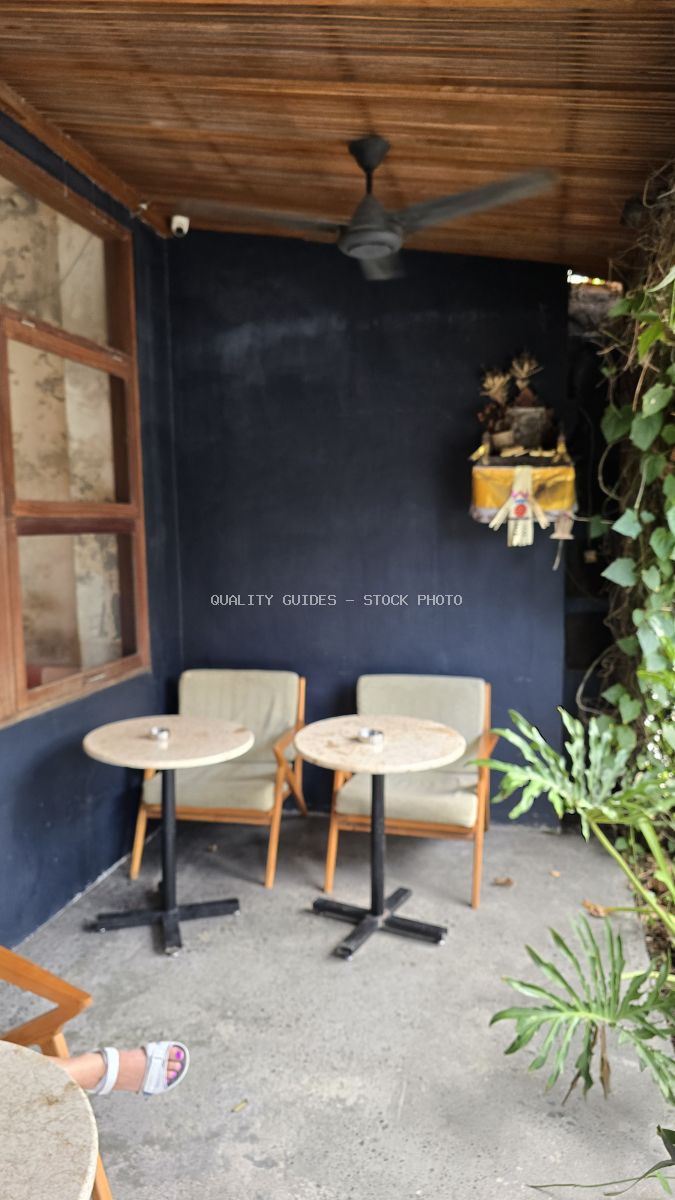 Outdoor cafe seating in Bali with two tables, chairs, a ceiling fan, and tropical plants. - stock photo