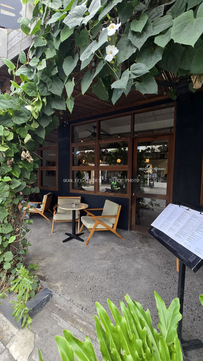 Exterior of Neighbourhood Food cafe in Bali with outdoor seating, green vines, and wooden windows. - stock photo