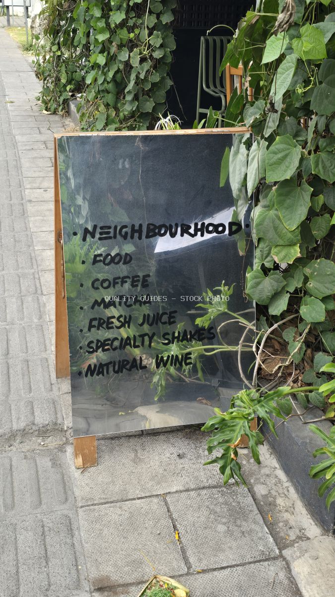 Reflective A-frame sign for Neighbourhood Food cafe on a Bali sidewalk, surrounded by green plants. - stock photo