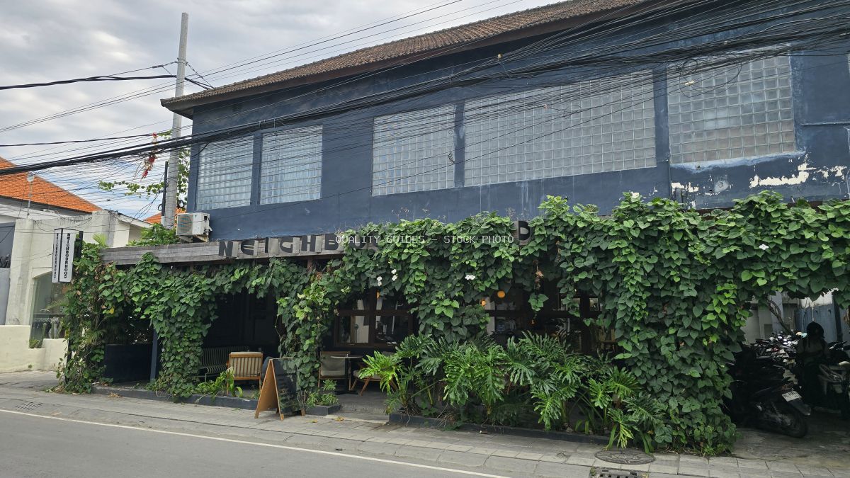 Exterior of Neighbourhood Food cafe in Bali, covered in green vines with a dark blue facade and glass block windows. - stock photo