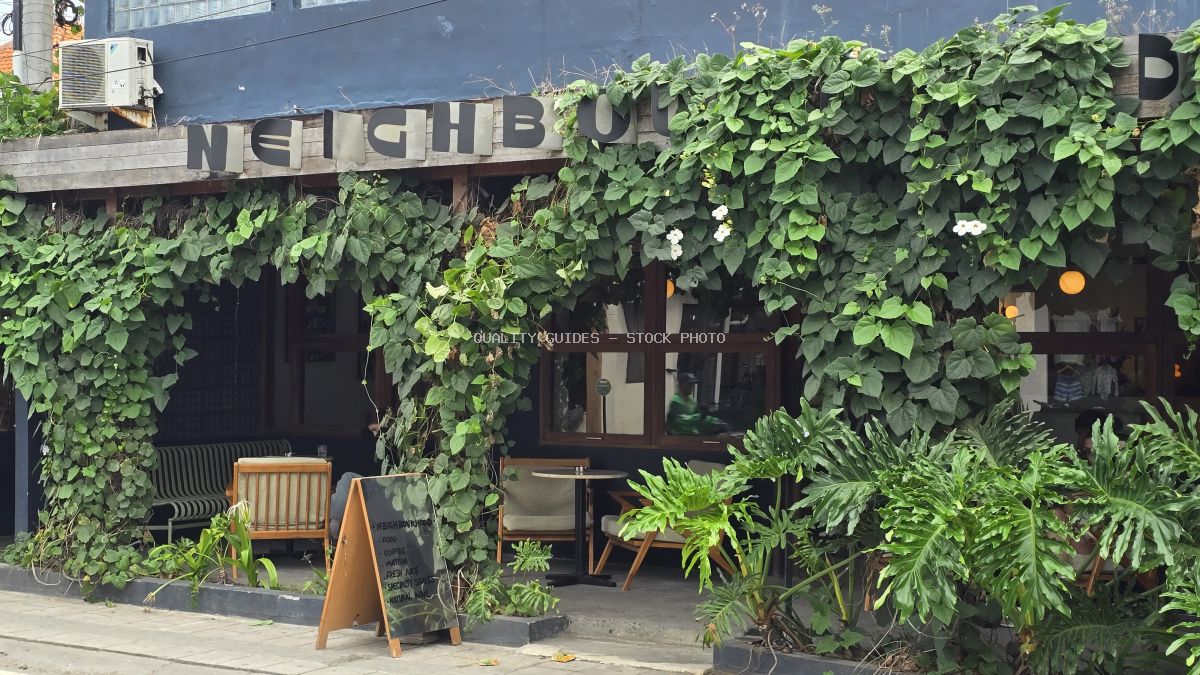 Exterior of a cafe in Bali covered in lush green vines, with outdoor seating and a chalkboard sign. - stock photo