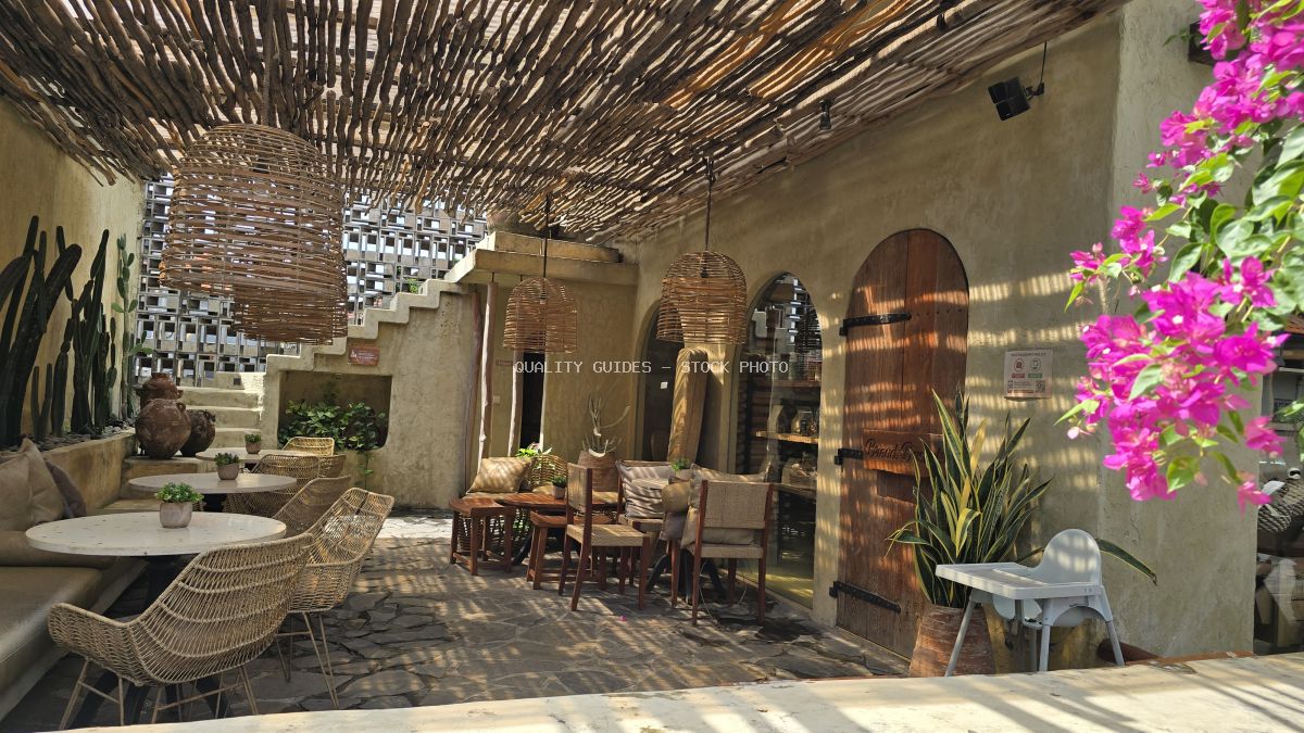 Rustic outdoor cafe in Bali with woven ceiling, wicker chairs, concrete walls, and vibrant pink bougainvillea. - stock photo