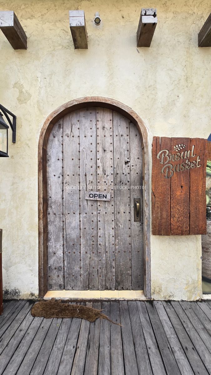 Rustic wooden arched door with 'OPEN' sign and 'Bread Basket' sign on a textured wall. - stock photo