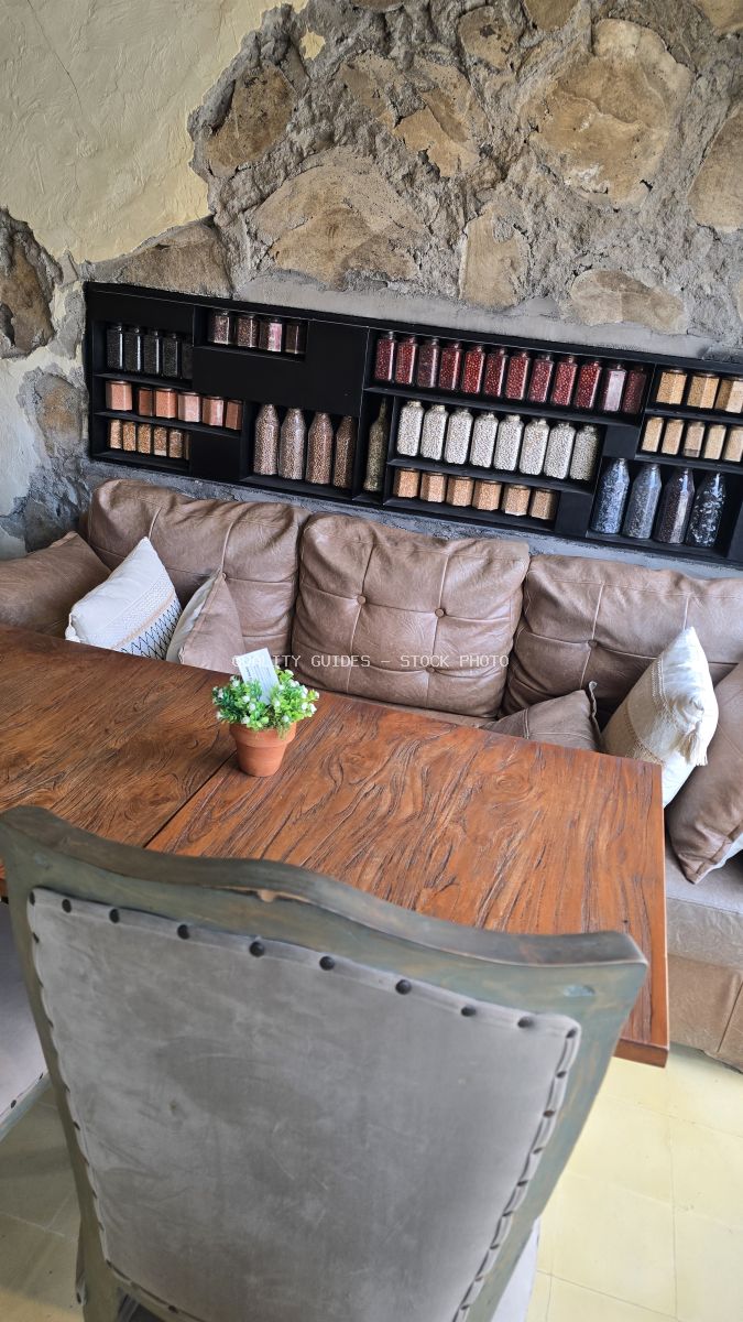 Rustic cafe interior with wooden table, leather bench, stone wall, and jars of grains. - stock photo