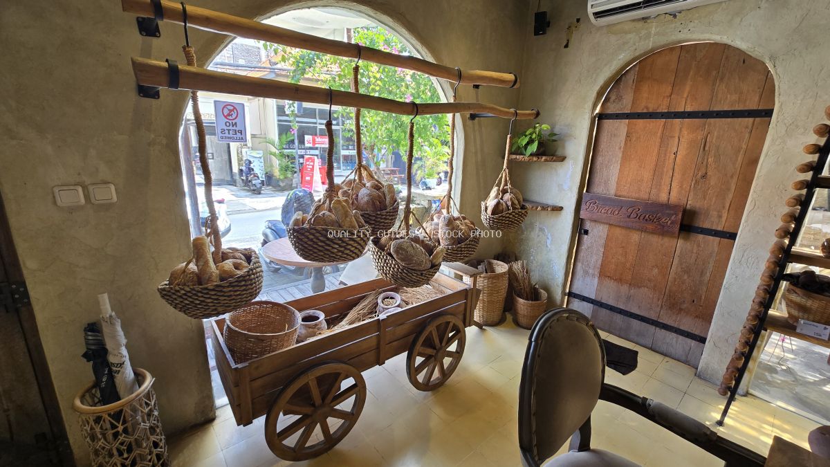 Interior of a rustic bakery with artisan bread in hanging baskets and a wooden cart, 'Bread Basket' sign on a wooden door. - stock photo