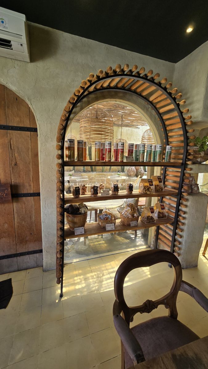 Interior of a rustic bakery in Bali with an arched wooden and metal display shelf holding artisanal food products, a wooden door, and a chair. - stock photo