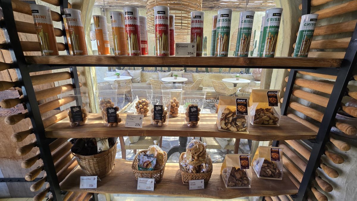 Bakery display with grissini, packaged snacks, and baked goods on wooden shelves in a Bali cafe. - stock photo
