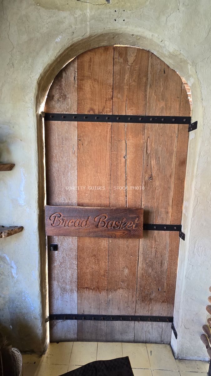 Rustic wooden arched door with a 'Bread Basket' sign in a stucco archway. - stock photo