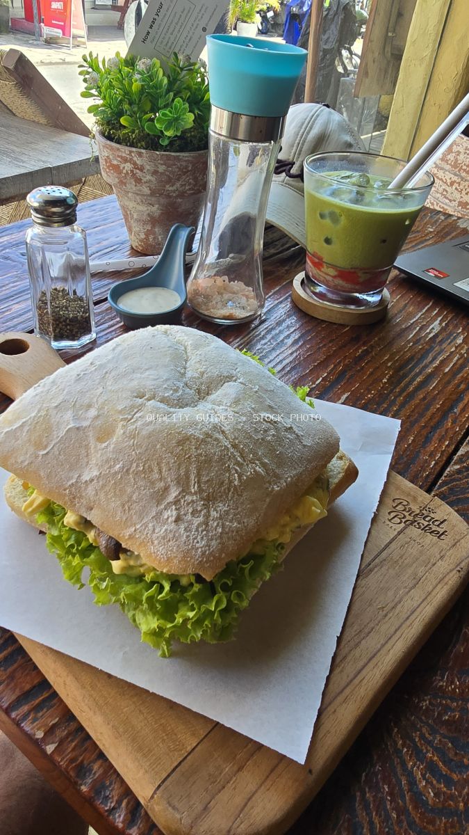 Ciabatta sandwich with lettuce and a layered green drink on a wooden table at Bread Basket Bakery. - stock photo