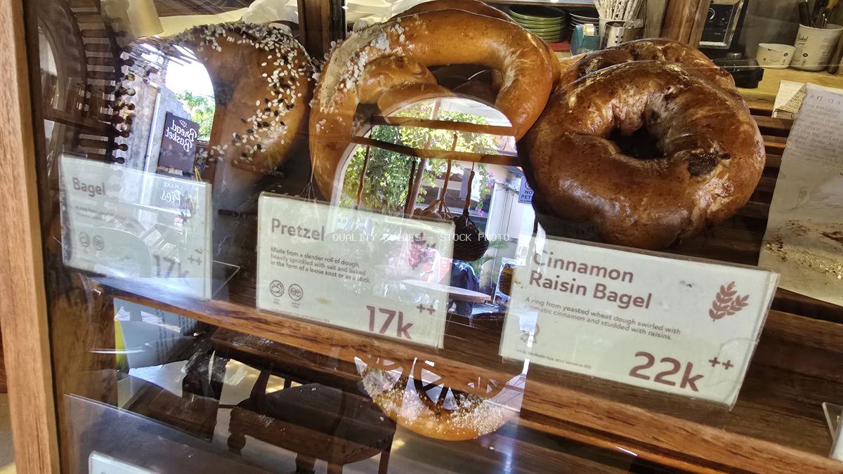 Assortment of bagels and a pretzel displayed in a glass bakery case with price tags. - stock photo