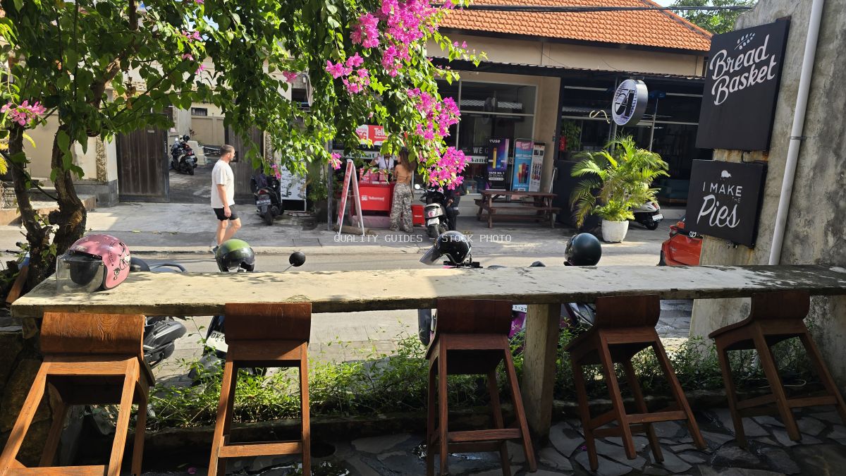 Outdoor cafe seating in Bali with a bakery, street, scooters, and bougainvillea flowers. - stock photo