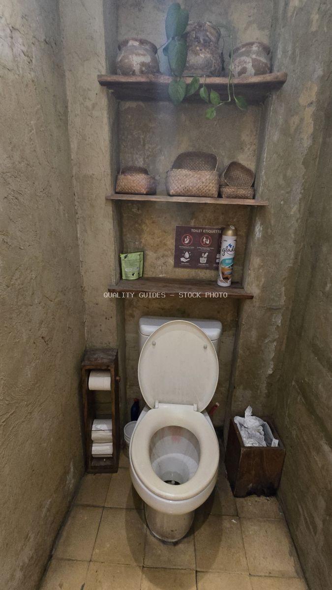 Rustic toilet interior with textured walls, wooden shelves, woven baskets, and a toilet paper holder. - stock photo