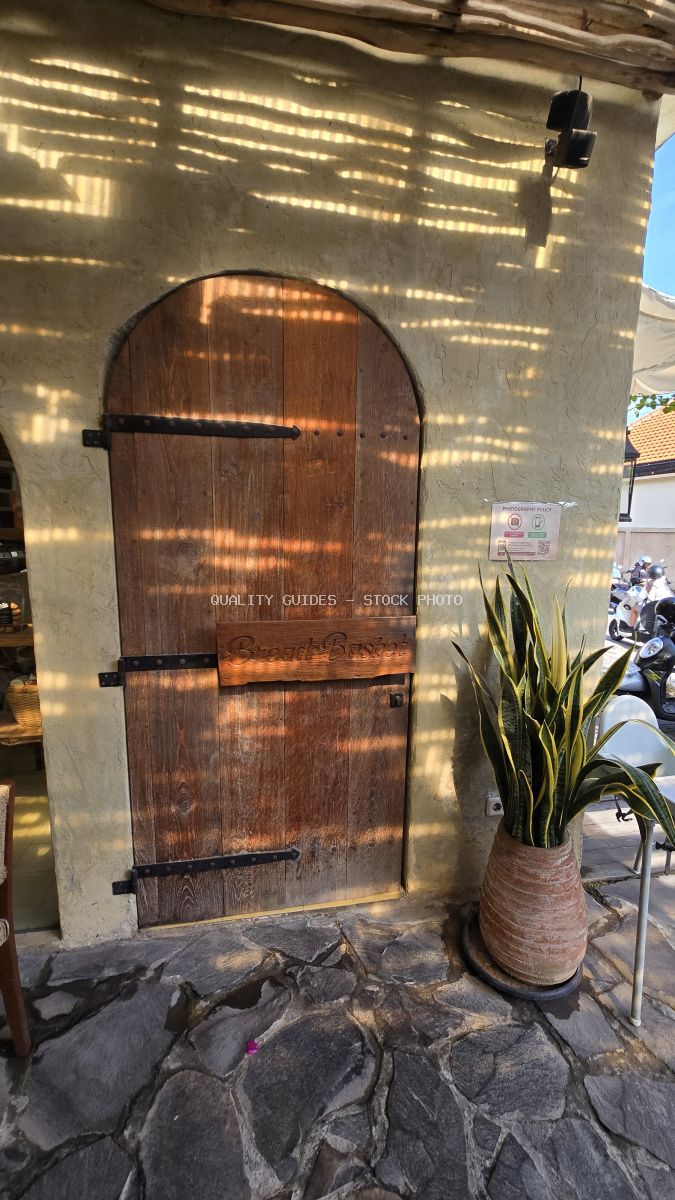 Rustic wooden arched door of Bread Basket Bakery in Bali with striped sunlight and a potted snake plant. - stock photo