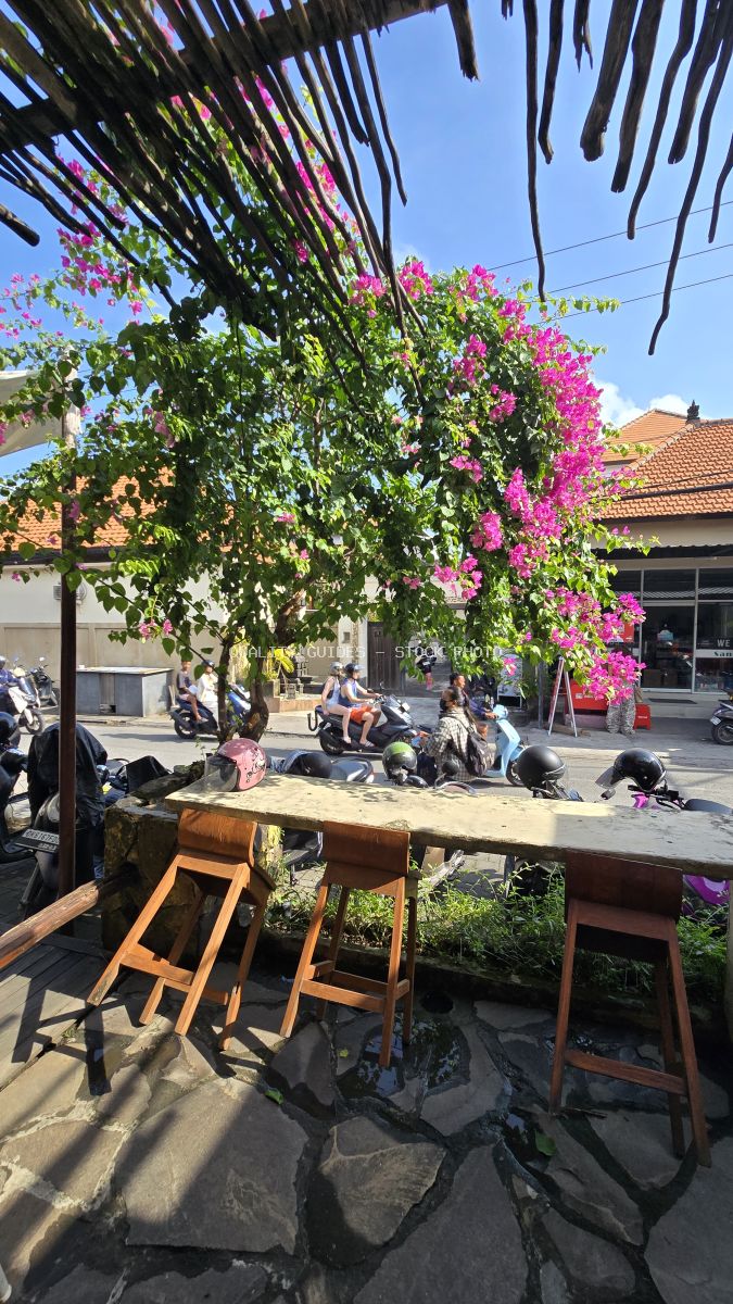 Outdoor cafe in Bali with pink bougainvillea, motorbikes on a sunny street. - stock photo