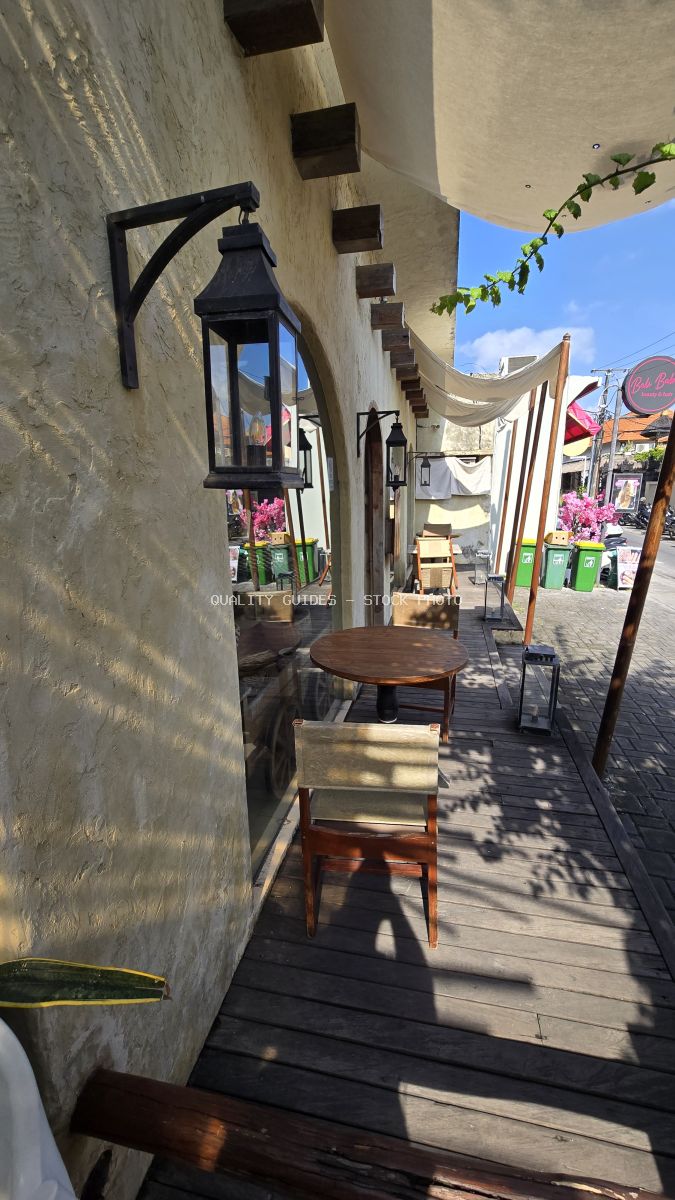 Outdoor cafe seating with a wooden table and chair, rustic lantern, and sunlit textured wall in Bali. - stock photo