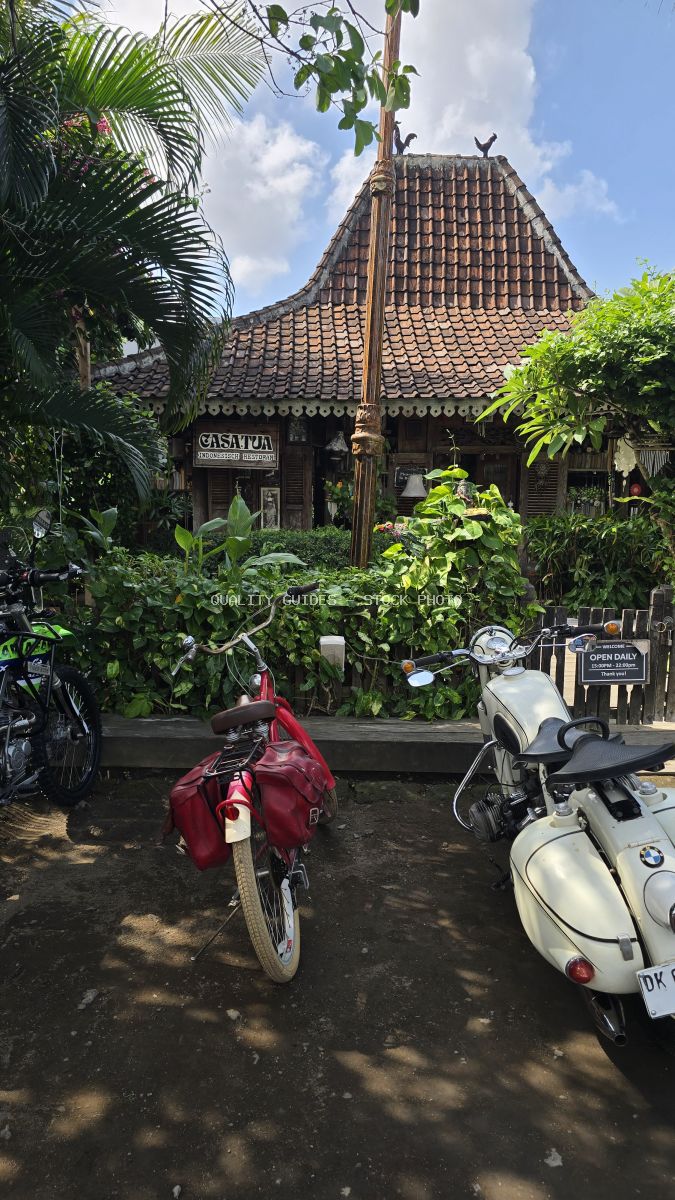 Exterior of Casa Tua Canggu cafe in Bali with traditional architecture, tropical plants, a bicycle, and a vintage motorcycle. - stock photo