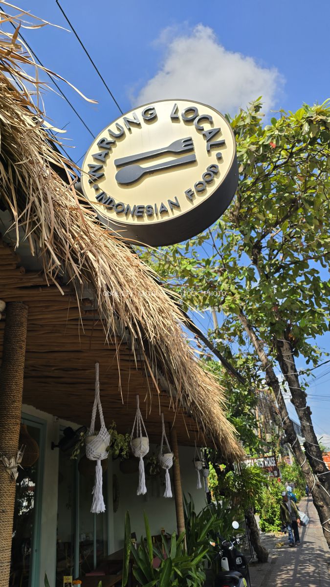 Exterior view of Warung Local Indonesian Food restaurant sign with thatched roof and tropical plants in Bali. - stock photo