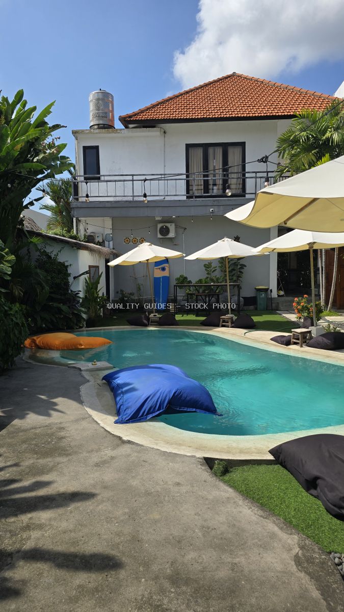 Sunny outdoor swimming pool with floating bean bags and umbrellas at a tropical hostel in Bali. - stock photo