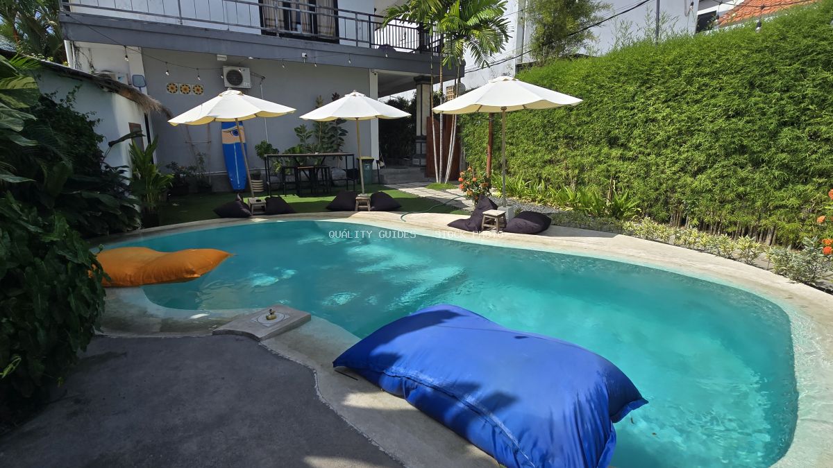 Outdoor swimming pool at a Bali hostel with bean bags, umbrellas, and tropical greenery. - stock photo