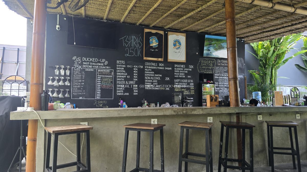 Open-air bar at What The Duck Backpackers in Bali with a detailed chalkboard menu, bar stools, and tropical plants. - stock photo