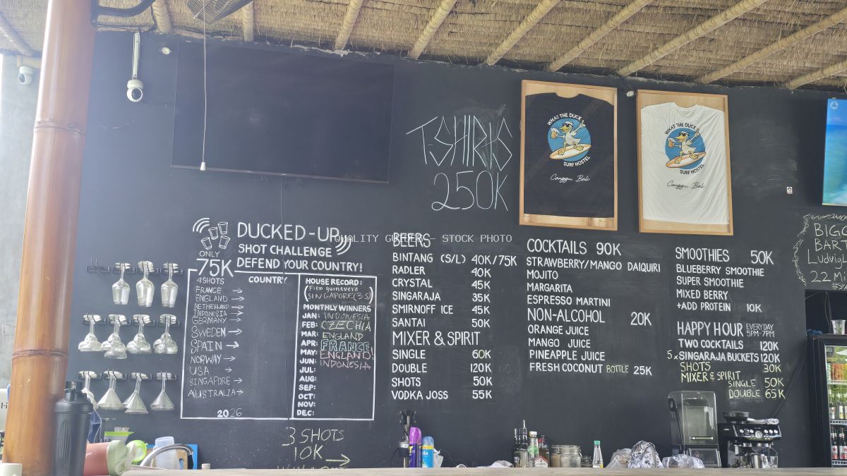 Chalkboard menu at What The Duck Backpackers bar in Bali, showing drink prices, a shot challenge, and branded T-shirts. - stock photo