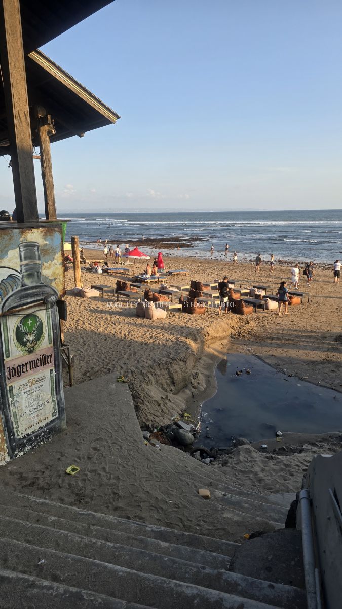 People relaxing at a beach bar on a sandy beach in Bali during golden hour, with the ocean in the background. - stock photo