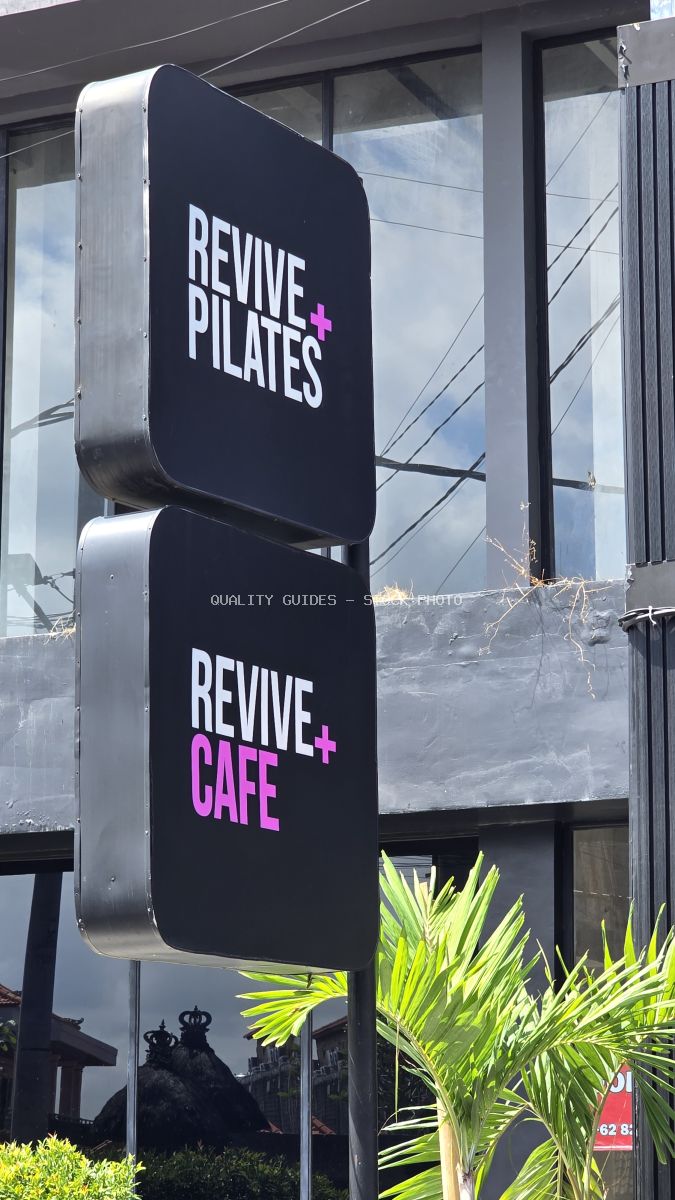 Black signs for Revive Pilates and Revive Cafe with white and pink text, set against a modern building with glass windows and palm leaves. - stock photo