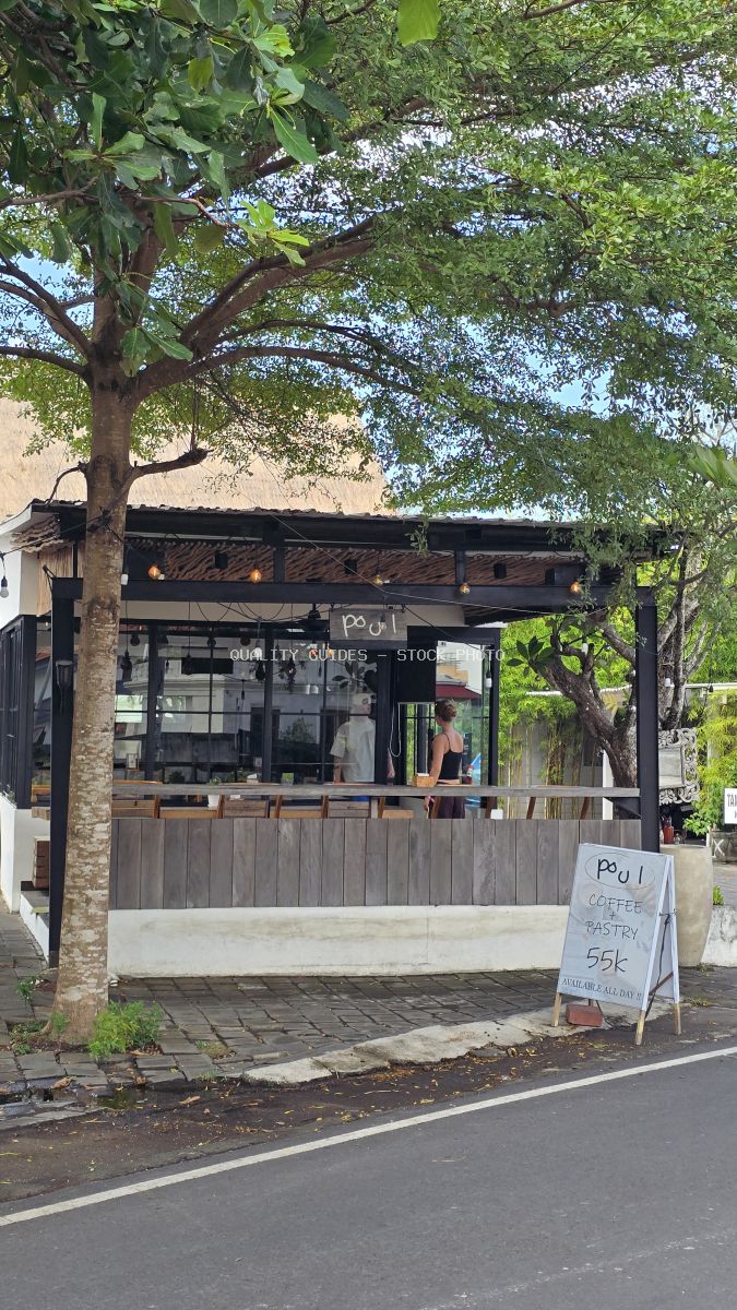Exterior of Poul Coffee & Pastry cafe in Bali with a large tree and sidewalk sign. - stock photo