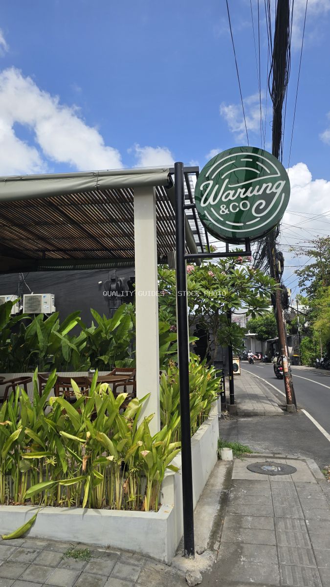 Exterior of Warung & Co cafe in Bali with green sign, tropical plants, and blue sky. - stock photo
