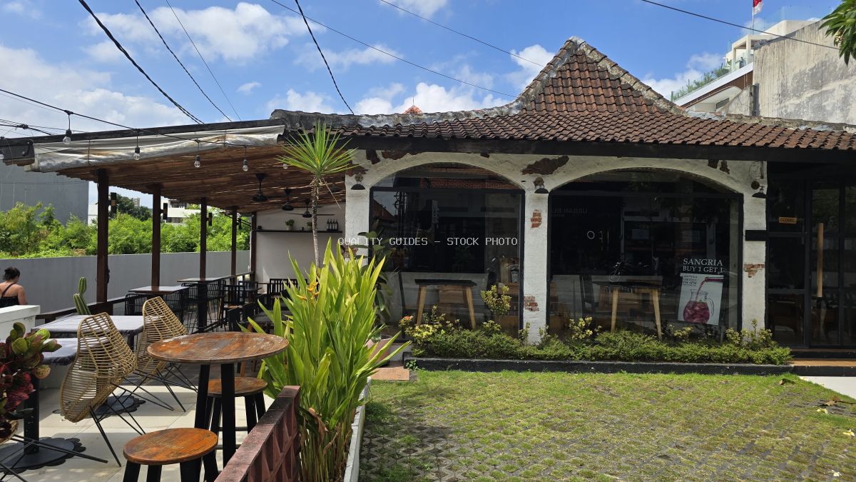 Exterior view of a tropical cafe in Bali with outdoor seating, traditional architecture, and lush greenery under a blue sky. - stock photo