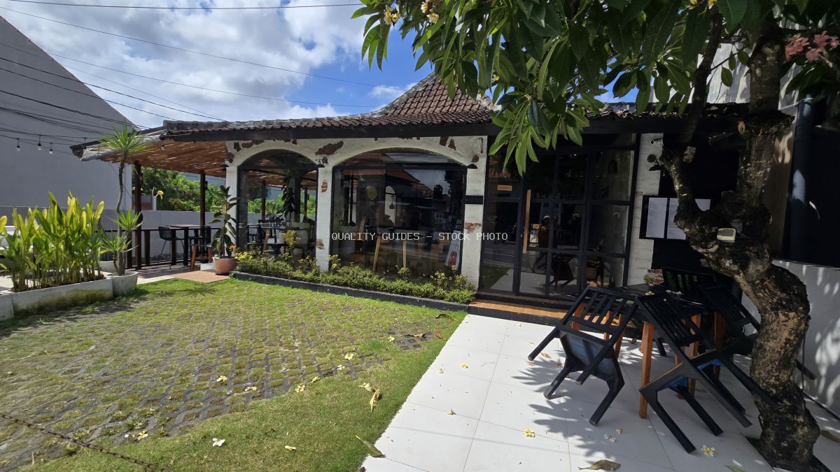 Exterior of Cantina Bali Canggu restaurant in Bali with traditional architecture, green lawn, and outdoor seating under a partly cloudy sky. - stock photo